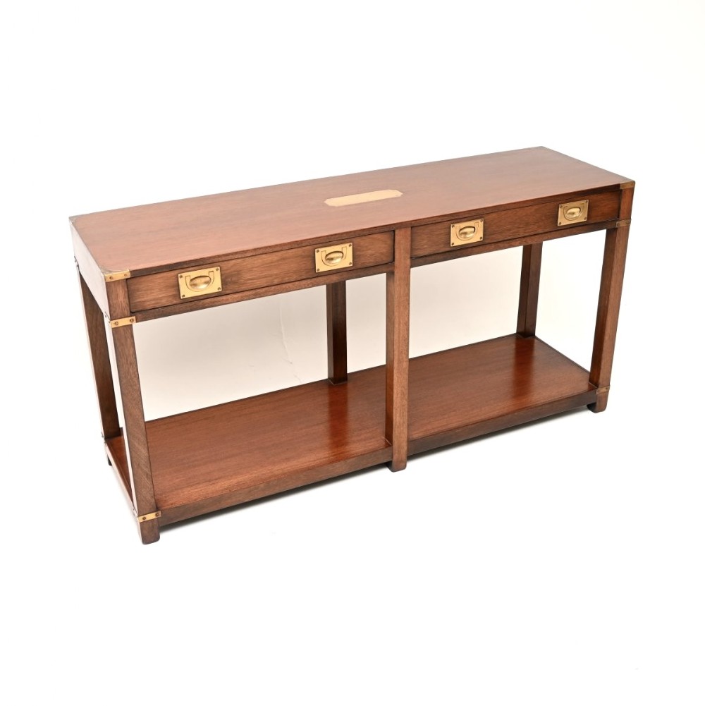 A military campaign style mahogany console table featuring flush brass corner brackets, brass recessed drawer handles, a central top brass plaque, and a lower open shelf.