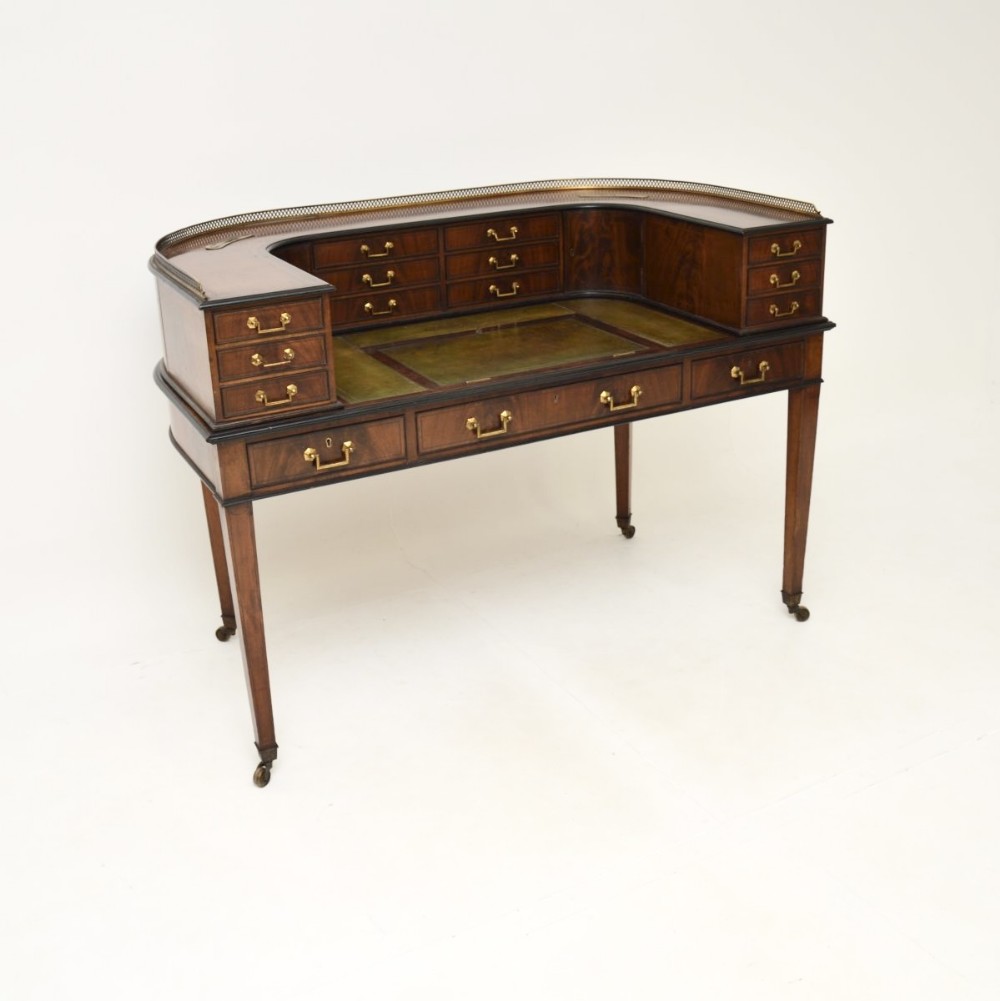 An antique inlaid mahogany Carlton House desk featuring a green leather writing surface, multiple small drawers arranged in a horseshoe shape, and a brass gallery rail.