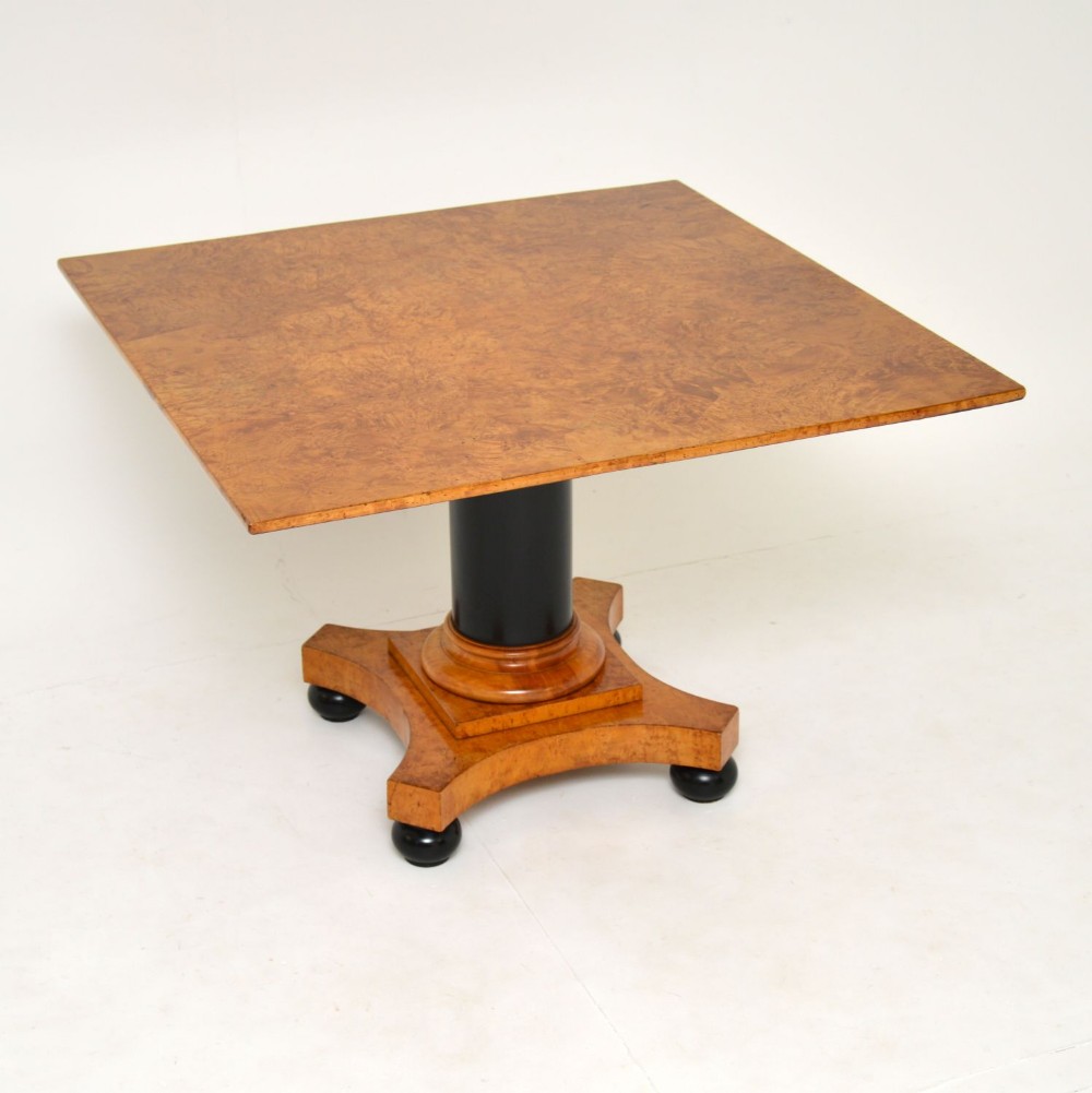A square Swedish Biedermeier coffee table featuring a figured golden birch veneered top supported by a central black ebonised column on a concave quadform base with ebonised ball feet.