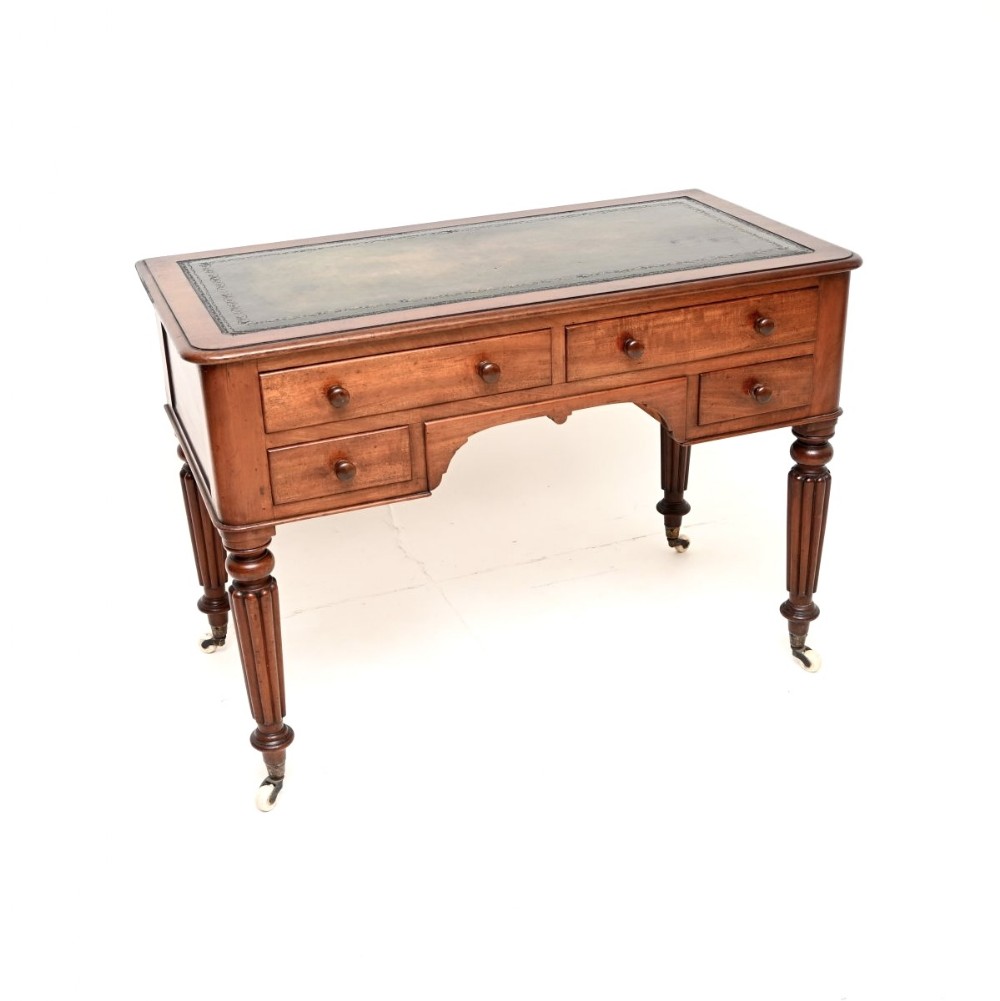 An antique Victorian mahogany writing desk featuring a green leather top insert, four drawers with turned wooden knobs, and fluted legs on ceramic castors.