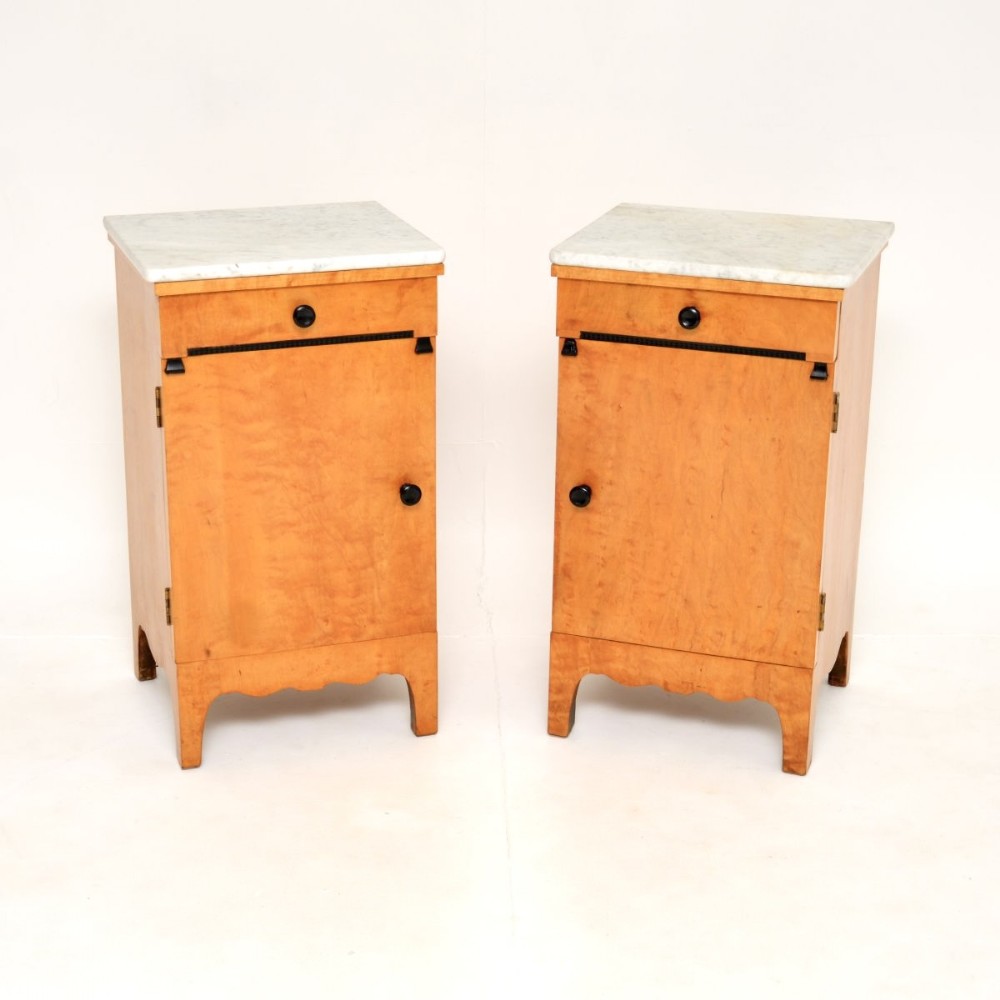 A matching pair of antique Swedish satin birch bedside cabinets with white marble tops, single drawers, and lower cupboard doors.