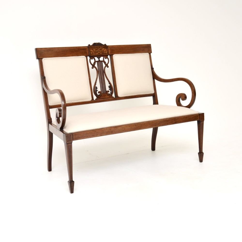 An Edwardian inlaid mahogany settee featuring a central lyre splat, sweeping armrests, cream fabric upholstery, and tapered square legs with spade feet.
