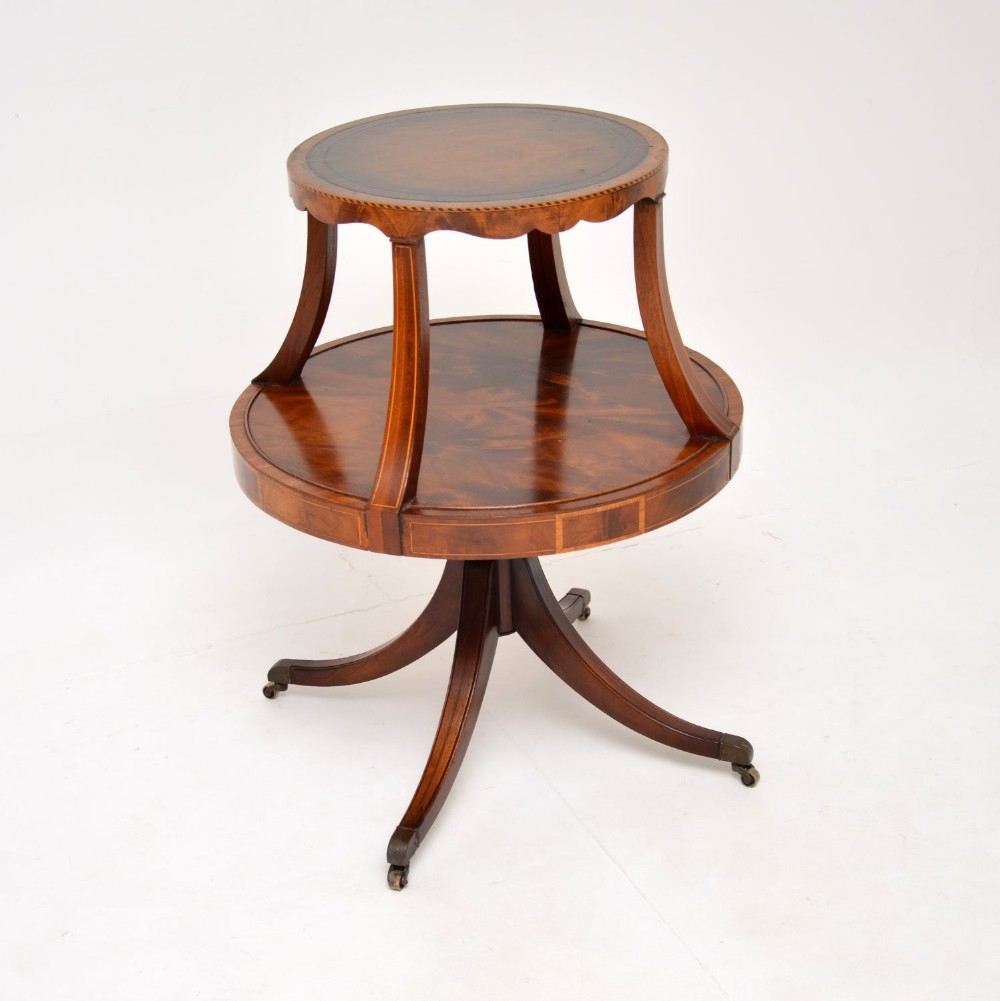 A Regency style mahogany two-tier occasional table with a leather inset circular upper top, lower mahogany tier, and splayed legs resting on brass castors.