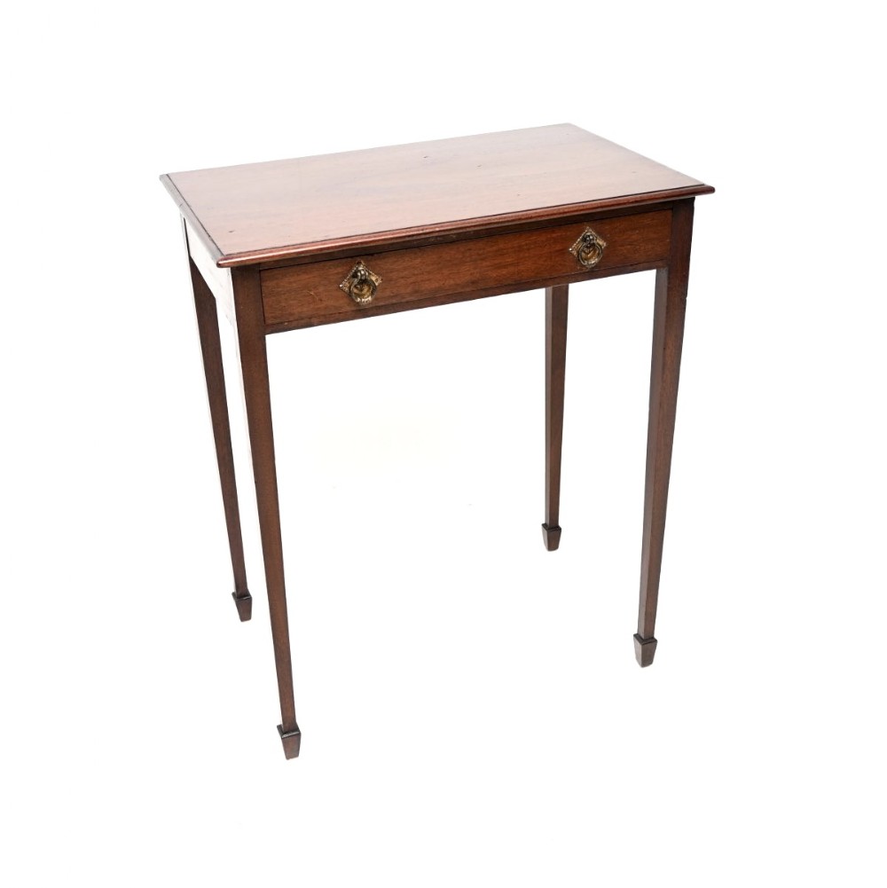 An Edwardian mahogany side table featuring a single drawer with twin brass handles and slender tapered legs ending in spade feet.