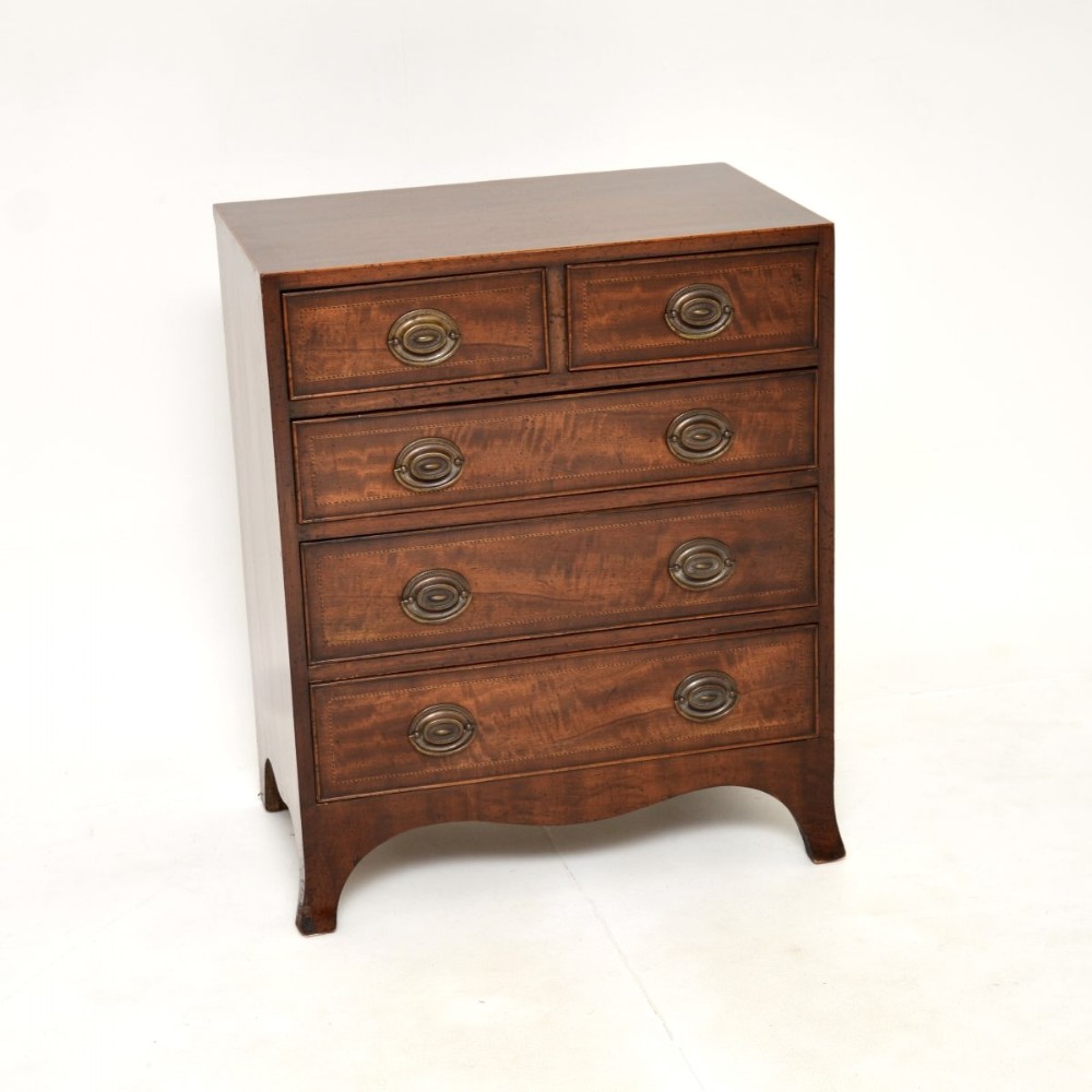 An antique mahogany chest of drawers featuring string inlay borders, five drawers with oval brass handles, and splayed bracket feet.