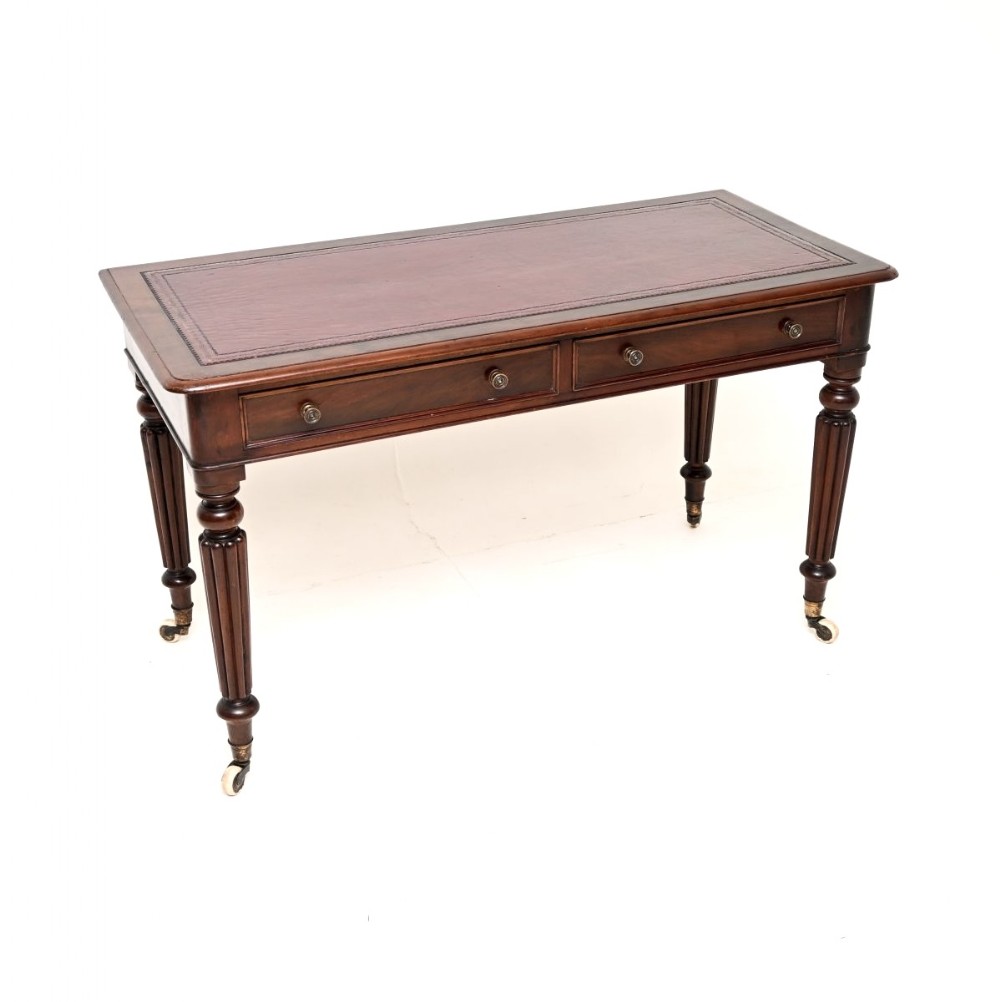 An antique Victorian mahogany writing table with a red leather top insert, two front frieze drawers, and reeded turned legs on brass castors.