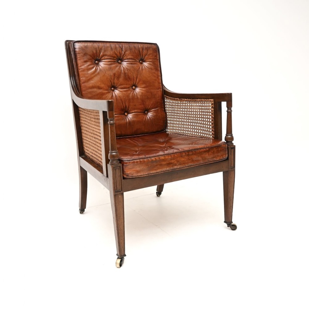 An Edwardian mahogany armchair featuring deep-buttoned brown leather cushions, woven cane side panels, and brass castors on tapered legs.