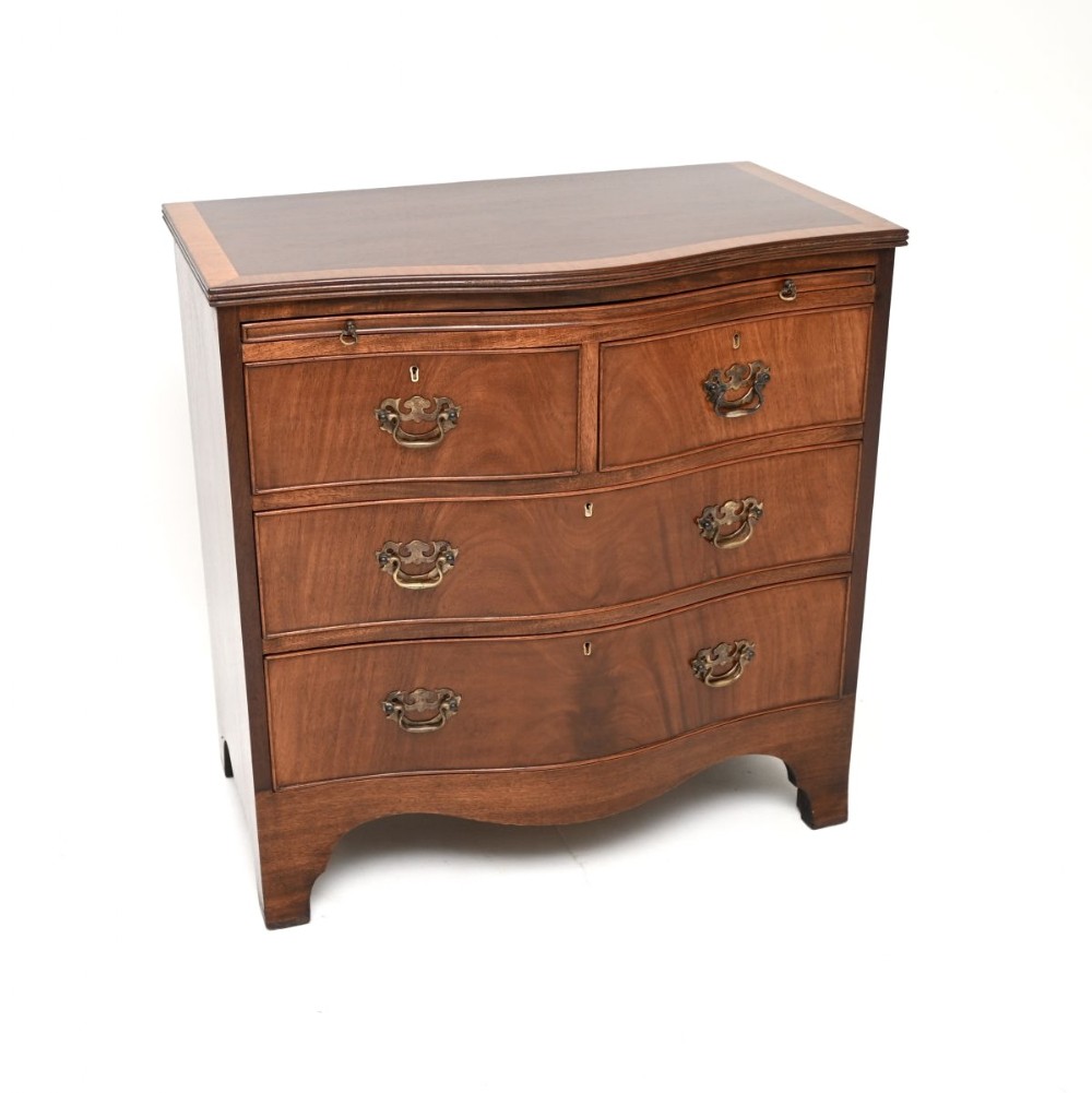 An Edwardian mahogany chest of drawers featuring a serpentine-front silhouette, four graduated drawers, brass swan-neck handles, and a pull-out brushing slide.