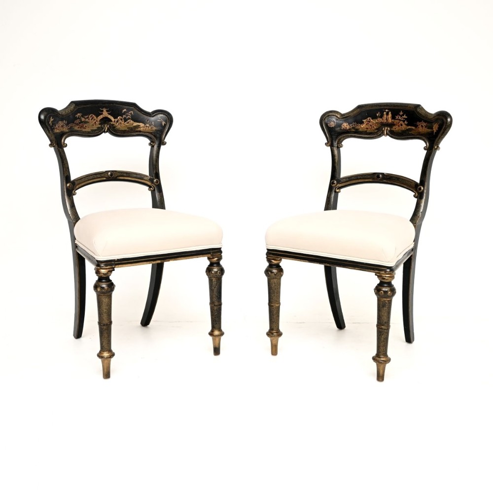 A pair of Victorian black lacquered side chairs featuring gilt Chinoiserie landscape painting on the backrests, turned front legs, and cream upholstered seats.