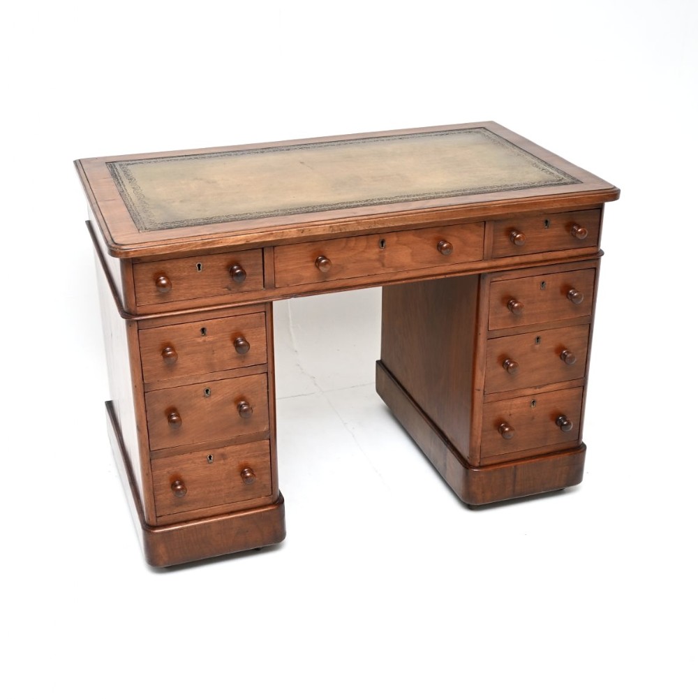 A Victorian walnut pedestal desk featuring nine drawers with turned wooden knobs and a green gilt-tooled leather writing surface.