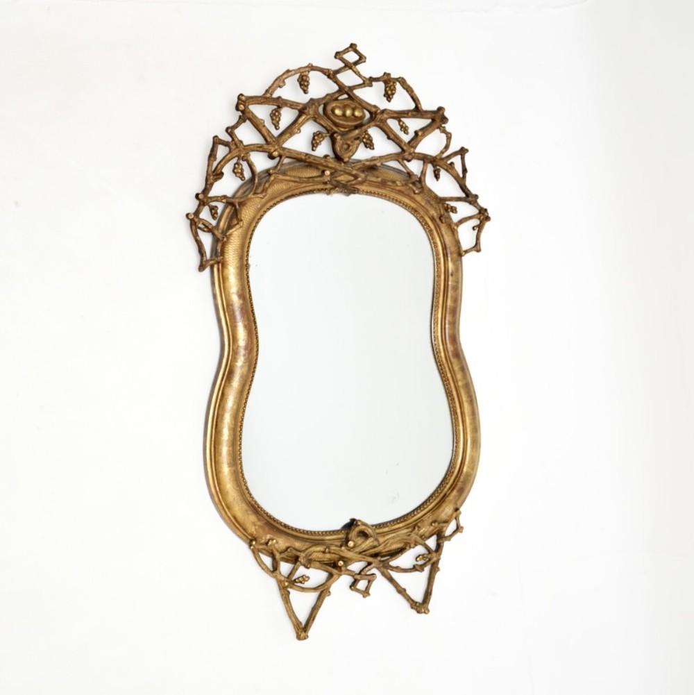 An antique Italian gilt wood wall mirror featuring an undulating frame crowned with carved vine and foliage cresting.