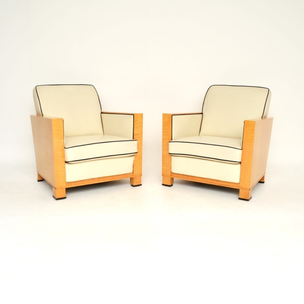 A pair of Swedish Art Deco armchairs with blonde satin birch side panels and cream leather upholstery detailed with black contrast piping.