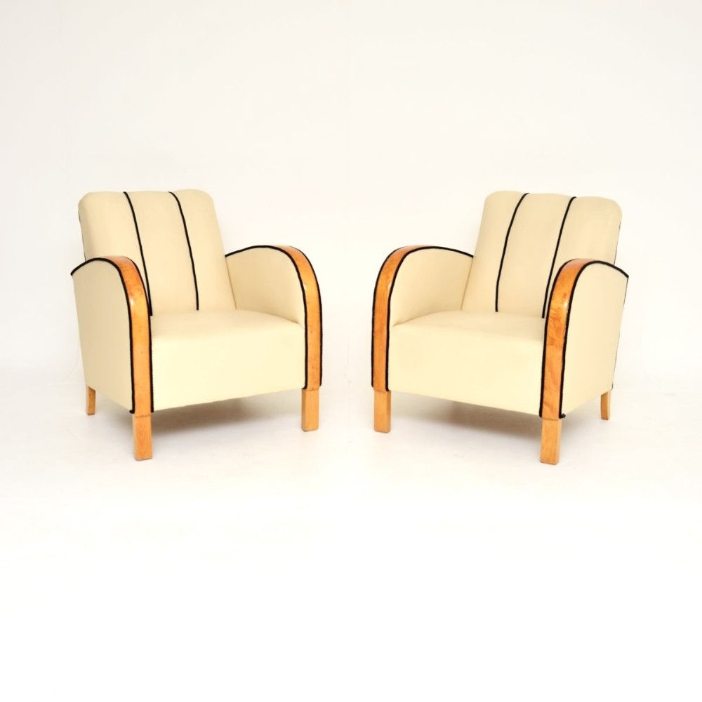 A pair of Swedish Art Deco armchairs upholstered in cream leather featuring curved satin birch armrests and black piping.