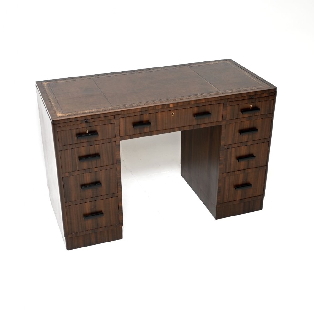 An Art Deco dark brown figured walnut pedestal desk featuring a leather insert top, nine drawers with dark linear handles, and keyhole escutcheons.