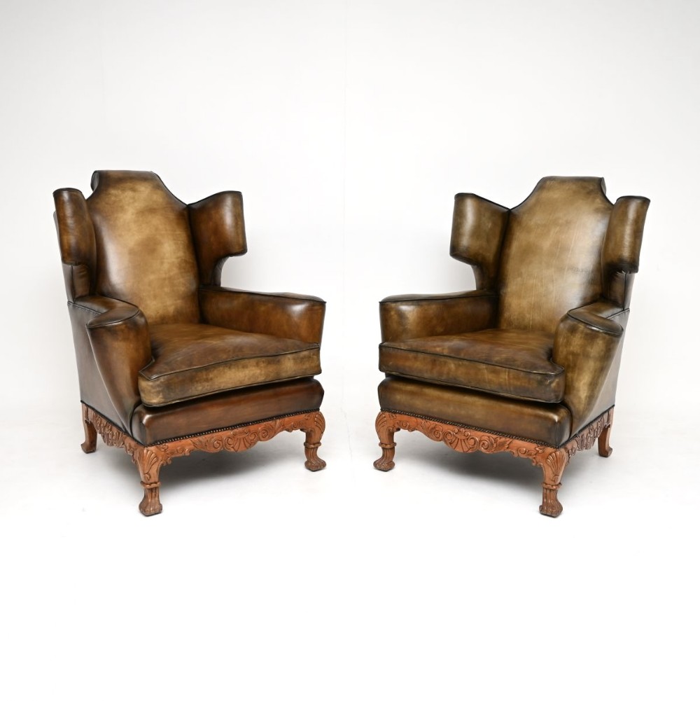 A pair of antique brown leather wingback armchairs with carved wooden aprons and cabriole legs.