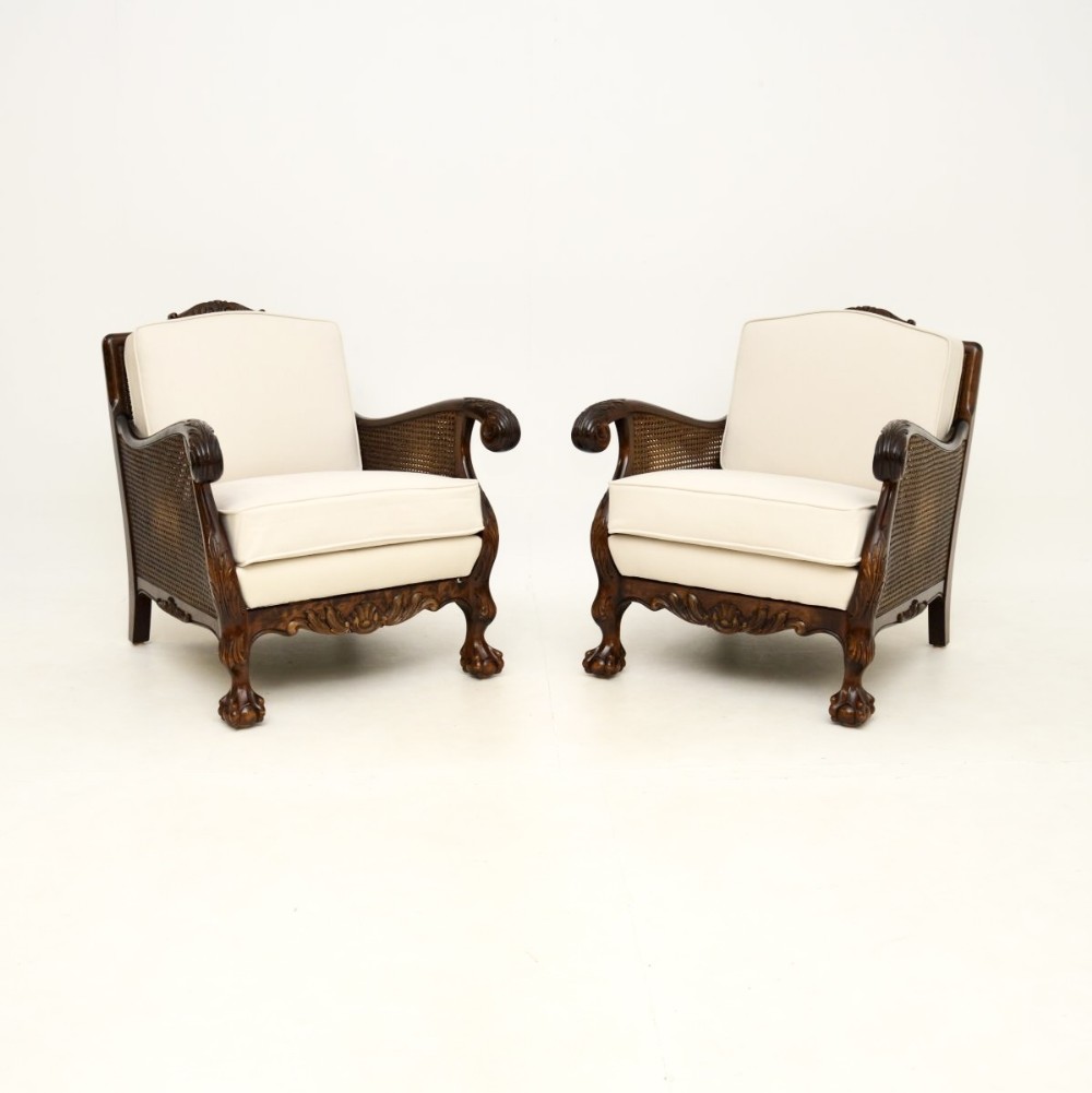 A pair of antique Swedish satin birch bergere armchairs featuring carved wood frames with claw and ball feet, caned side panels, and cream upholstered cushions.