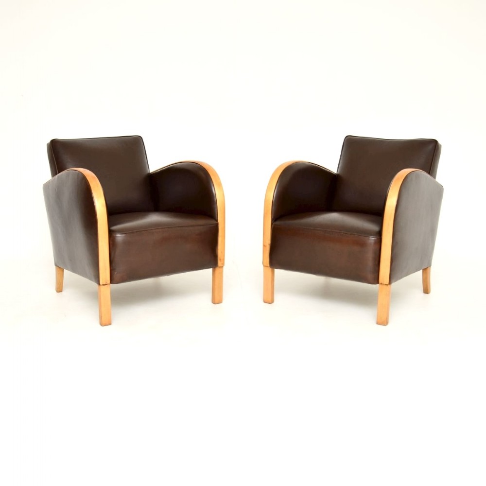 A pair of Art Deco armchairs featuring dark brown leather upholstery and sweeping curved satin birch wood armrests on square legs.