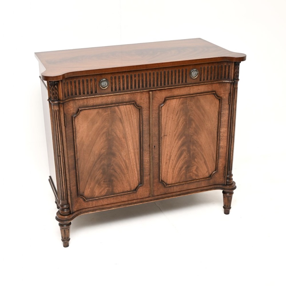 An antique flame mahogany two-door side cabinet featuring fluted corner columns, circular brass handles, and turned reeded legs.