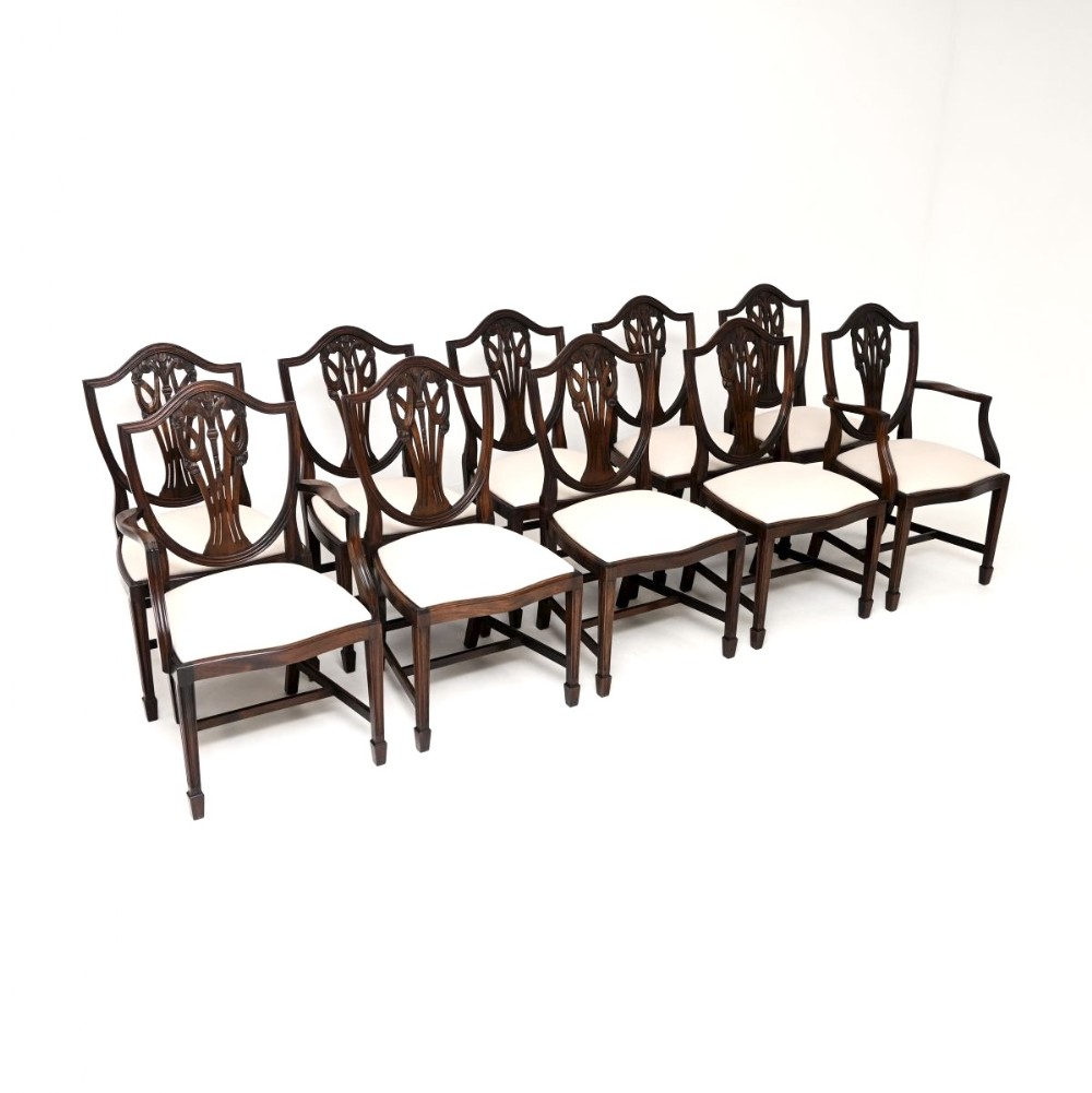 A set of ten dark mahogany shield back dining chairs with carved central splats and cream upholstered seats.