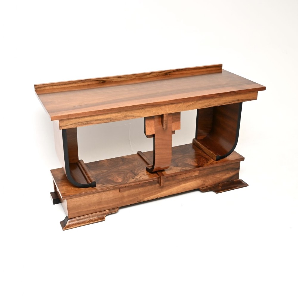 An Art Deco figured walnut console table featuring a rectangular top, curved ebonised side supports, a lower shelf base, and prominent timber graining.