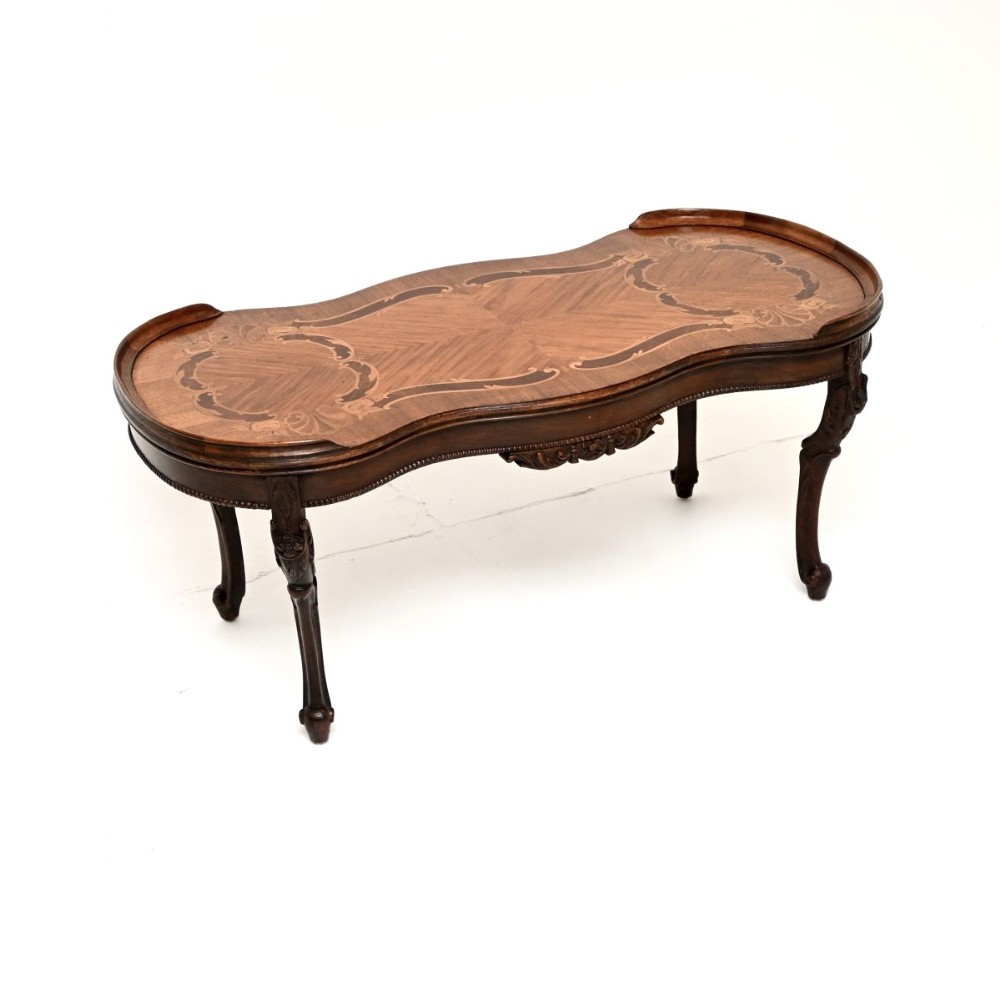 An antique French Louis XV style coffee table featuring intricate floral marquetry inlays, a shaped serpentine top with raised ends, and carved cabriole legs.