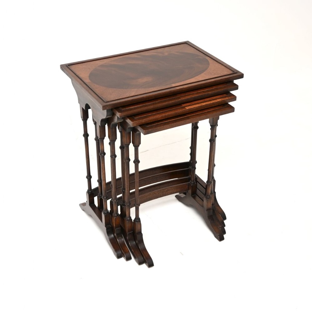 A set of four dark mahogany nested side tables featuring oval inlaid tabletops, turned spindle legs, and trestle feet.