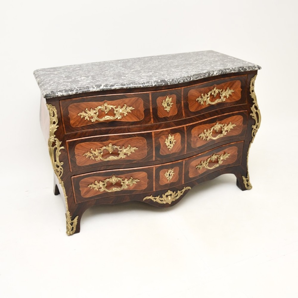 A French Louis XV bombee commode featuring dark wood marquetry veneers, ornate gilt-bronze mounts, three drawers, and a contoured grey veined marble top.