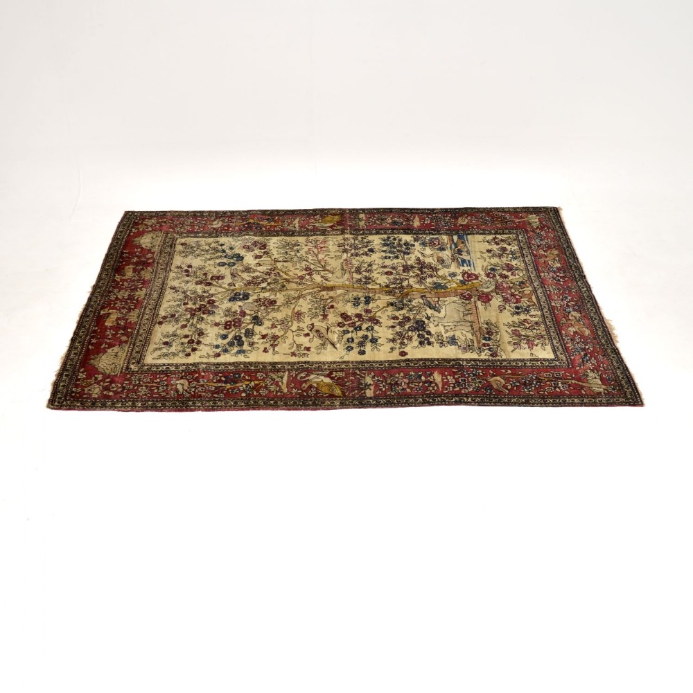 An antique Persian hand-knotted wool rug featuring a central Tree of Life motif on a cream field framed by a detailed crimson border.