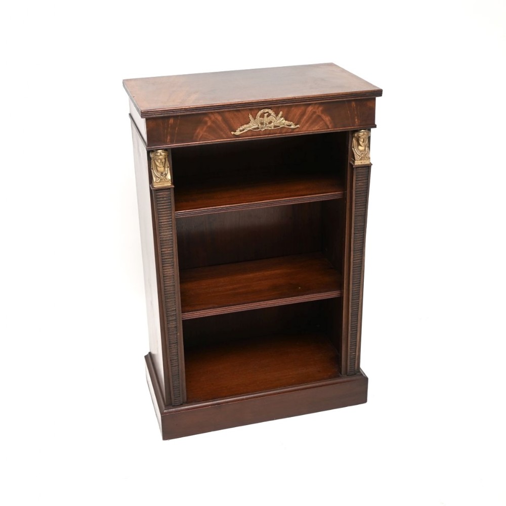 A dark mahogany Empire style open bookcase featuring three shelves flanked by fluted pilasters topped with female bust capitals and central gilt metal frieze decoration.
