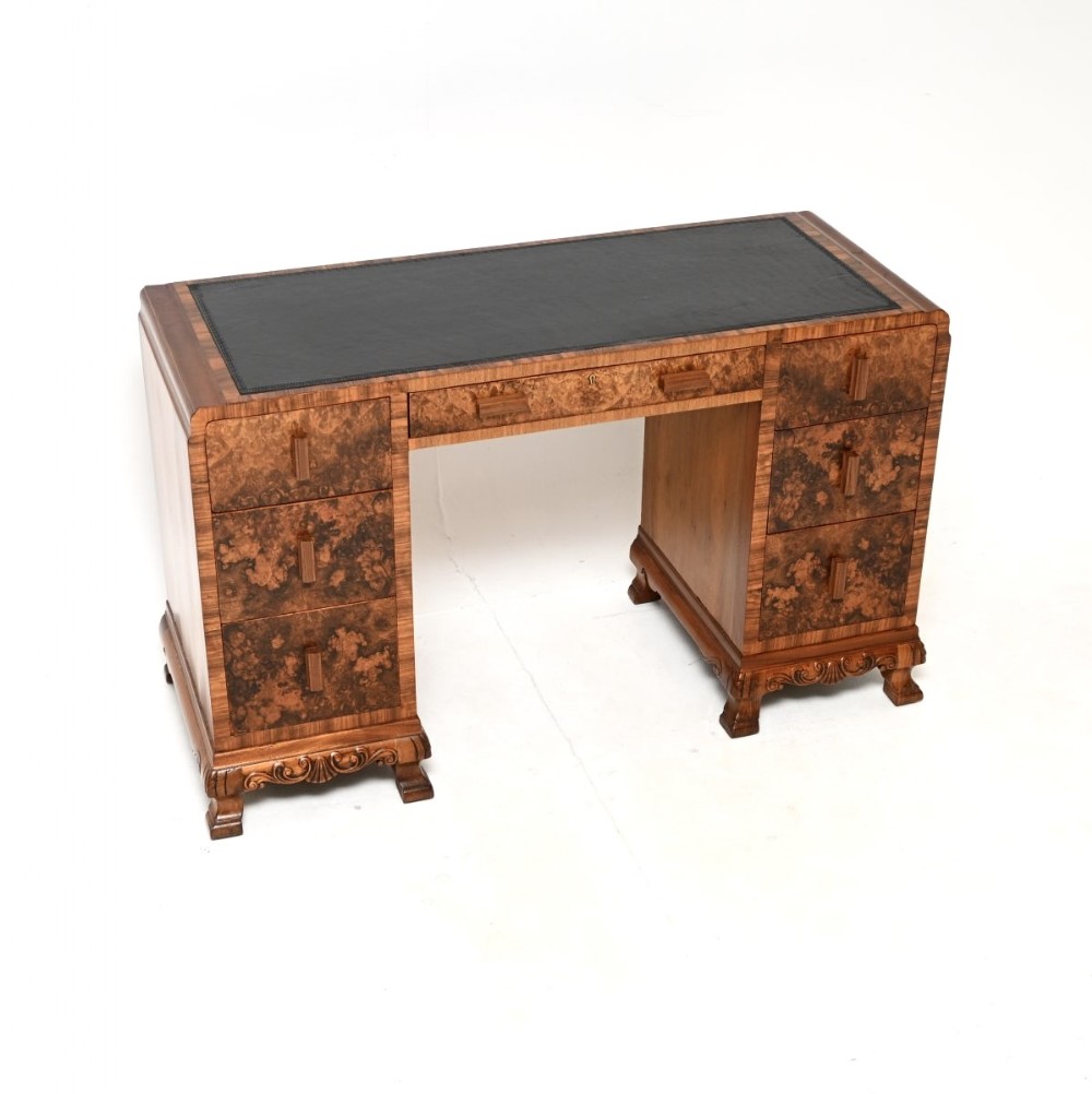 An Art Deco twin-pedestal writing desk featuring burr walnut veneer drawers, a black leather top insert, vertical wooden pulls, and carved bracket feet.