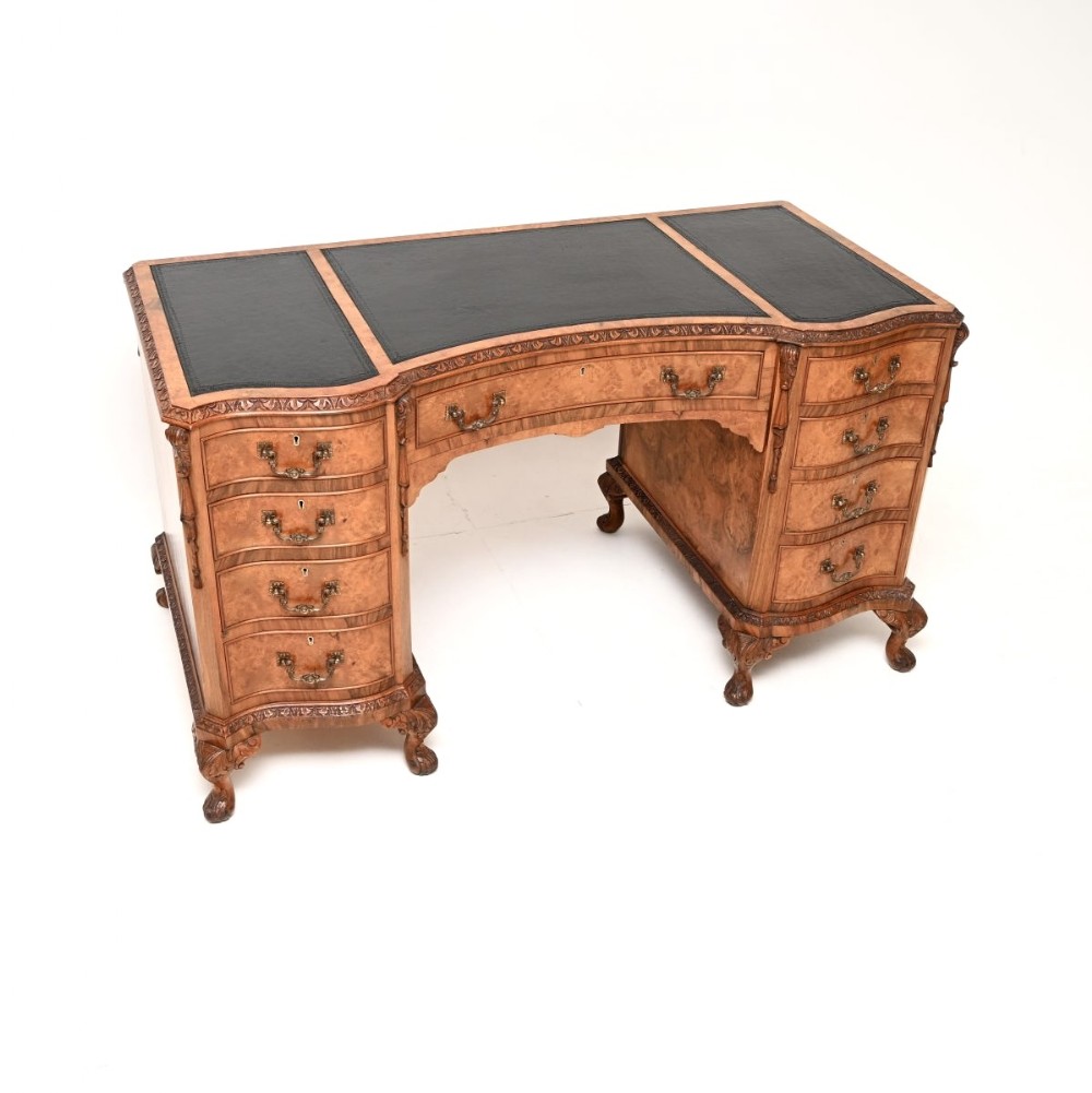 A curved burr walnut pedestal desk featuring a three-panel black leather writing surface, nine drawers with brass handles, carved trim, and cabriole legs ending in ball-and-claw feet.