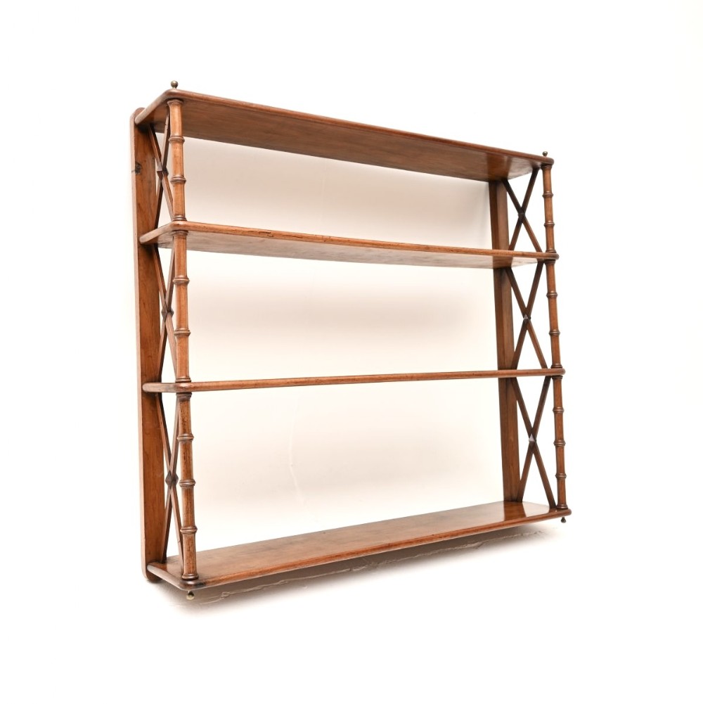 A Georgian period wall-mounted walnut bookcase featuring four open shelves, x-frame sides, and turned spindle supports.