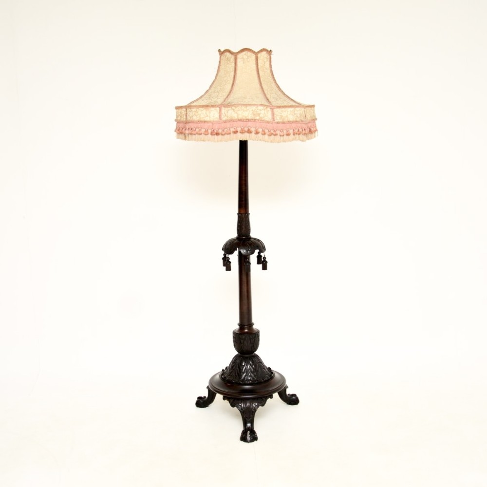 An antique Victorian carved mahogany standard lamp featuring a carved tripod base, turned column, and a light fabric shade with fringed edging.