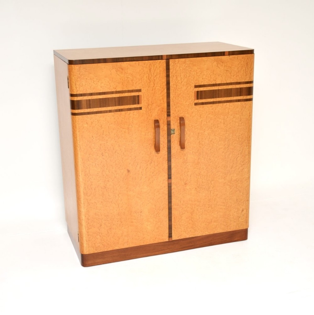 An Art Deco two-door compactum wardrobe crafted from birds eye maple veneer with contrasting dark walnut band details and wooden handles.