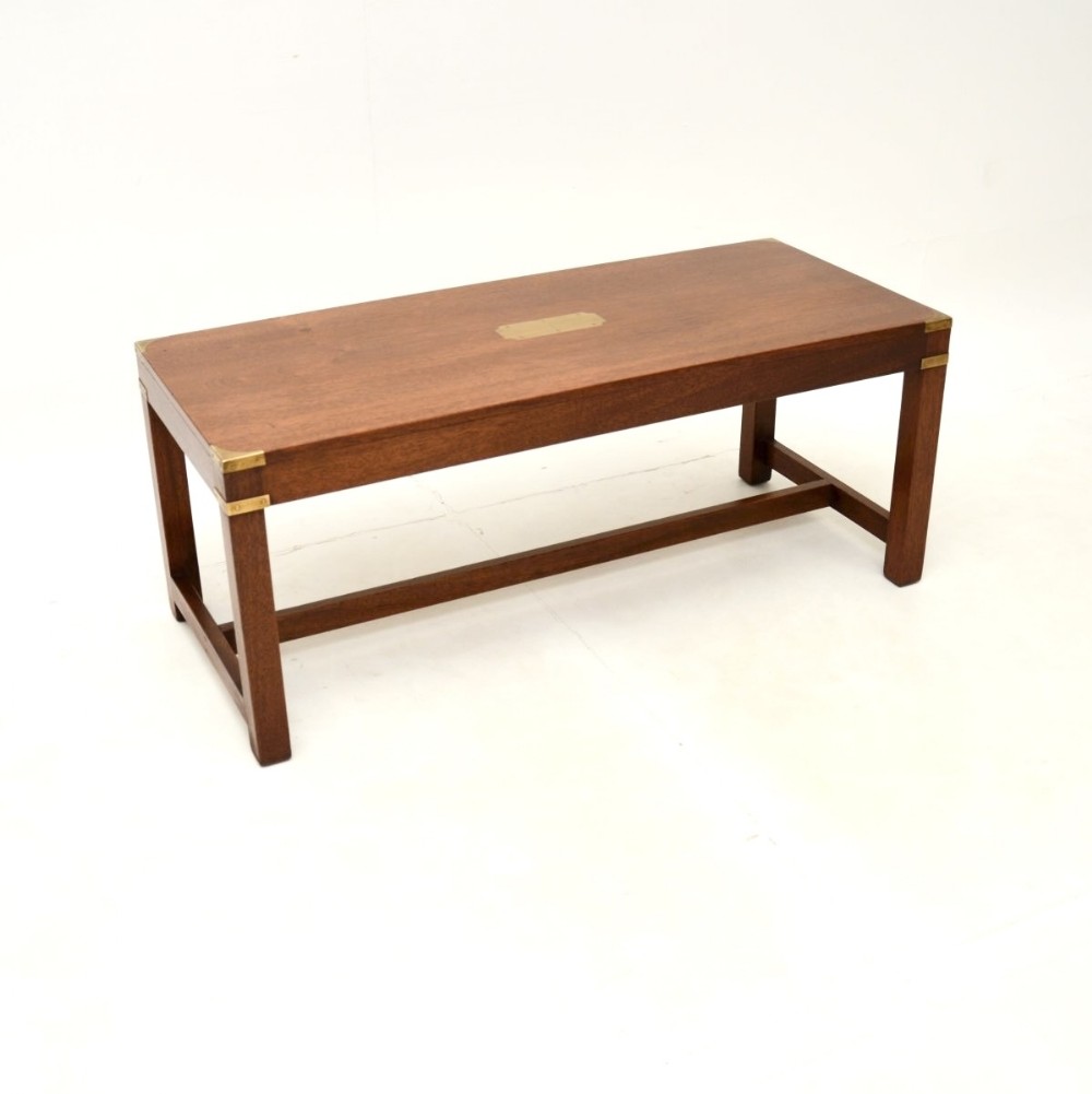A rectangular mahogany campaign style coffee table featuring protective brass corner brackets and a central brass inset plaque, supported by straight legs with a lower stretcher.