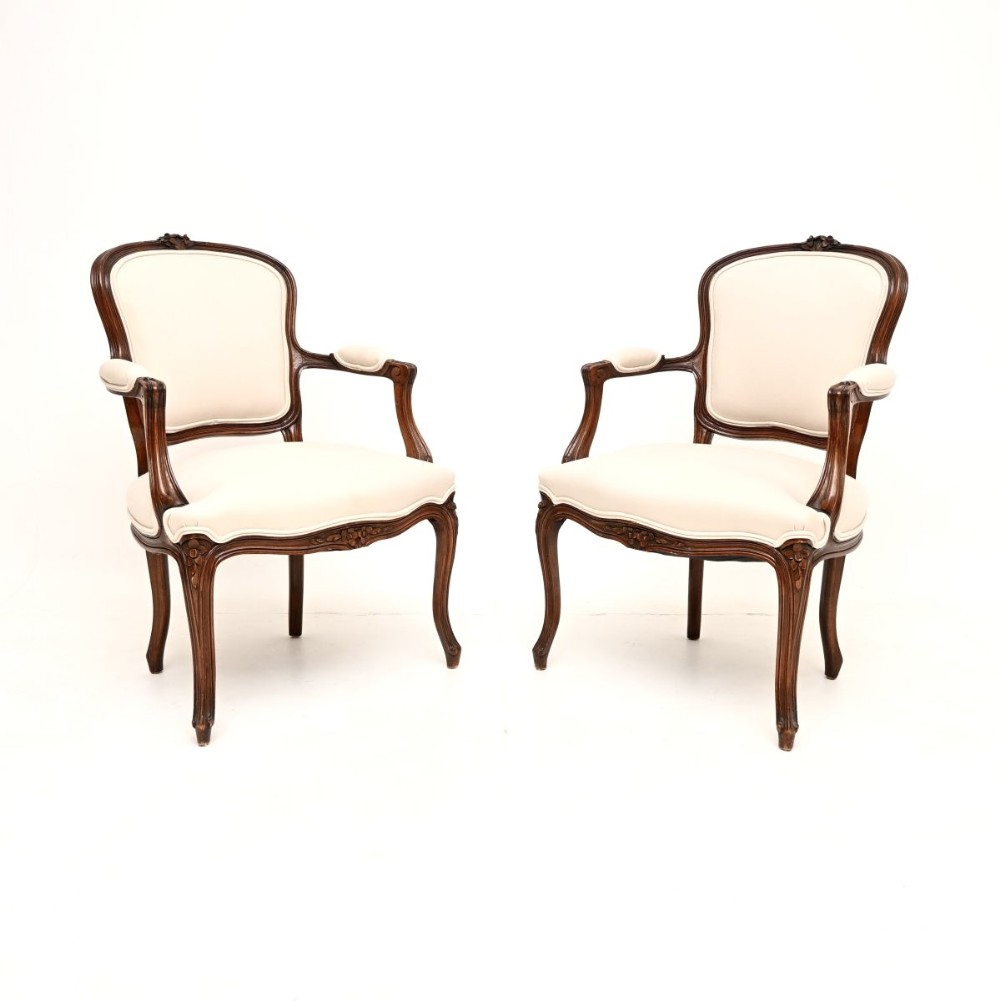 A pair of French Louis XV style carved walnut salon armchairs upholstered in cream fabric with cabriole legs.
