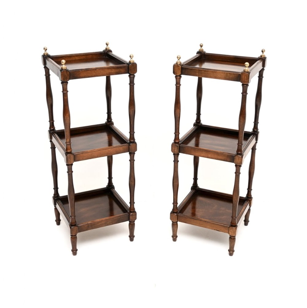 A matching pair of three-tier dark mahogany side tables with turned spindle supports and brass finials on the top corners.