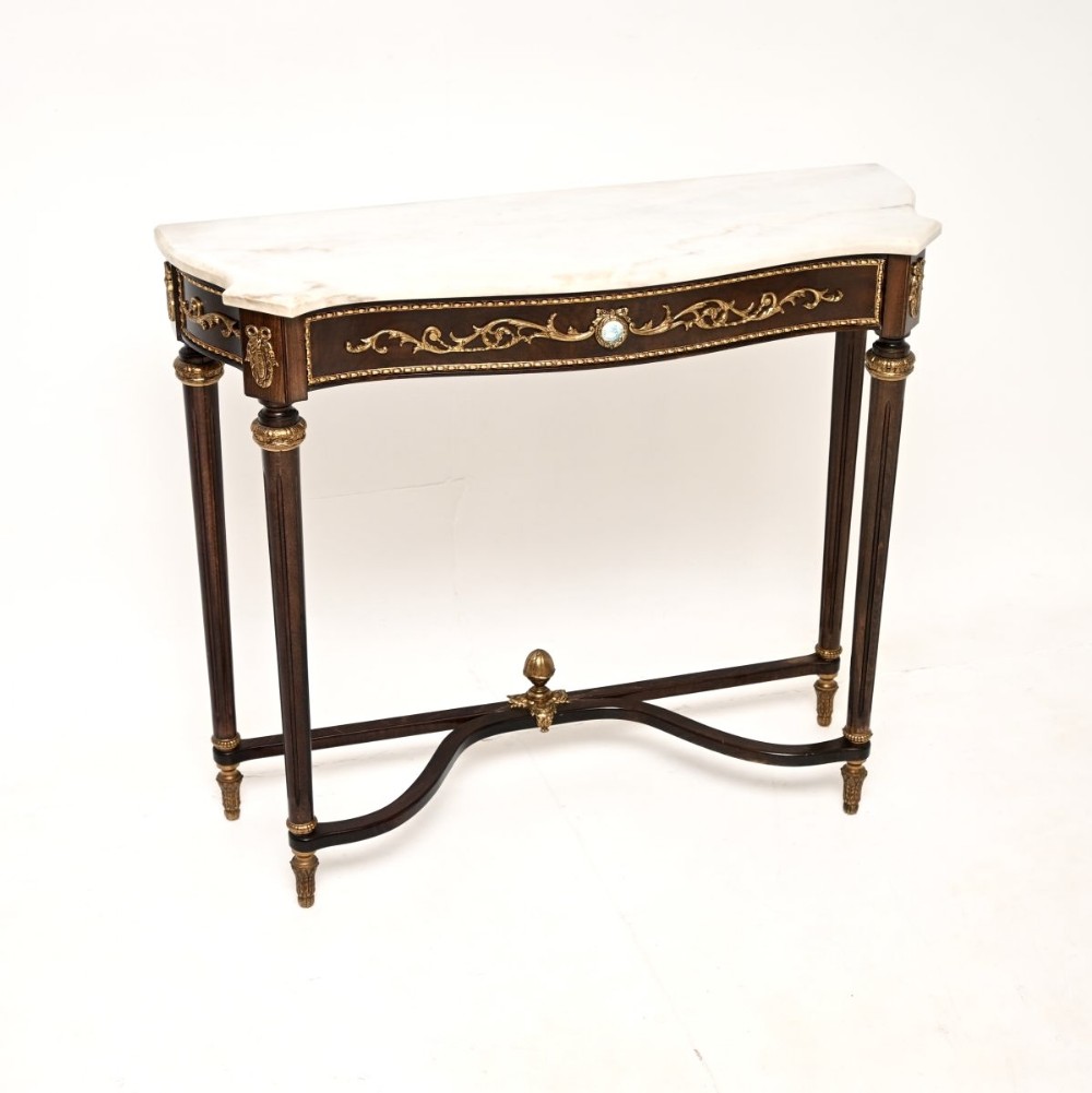 A French Louis XVI style walnut console table featuring a contoured white marble top, tapered fluted legs, gilt-bronze mounts, and a central porcelain plaque.