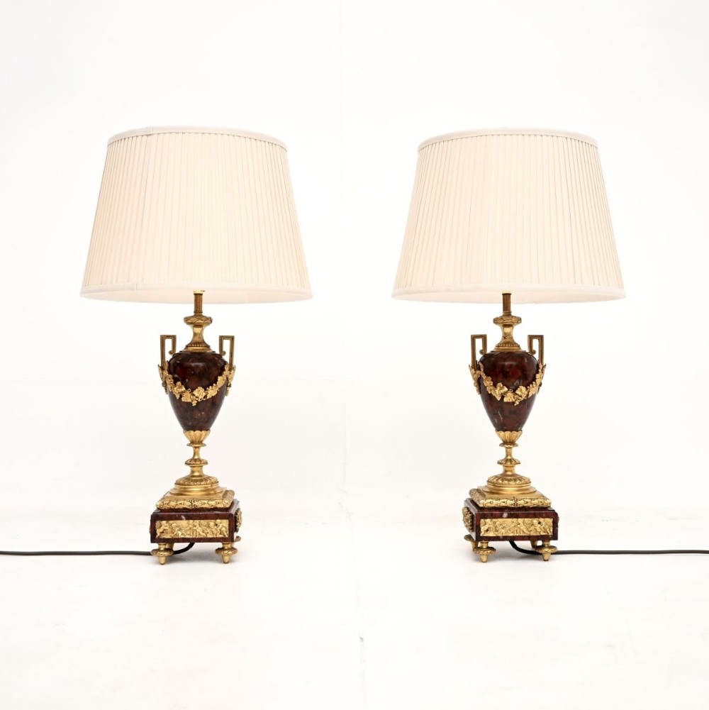 A pair of French Neoclassical table lamps crafted from dark red marble urns with gilt bronze foliage garlands and pleated cream shades.