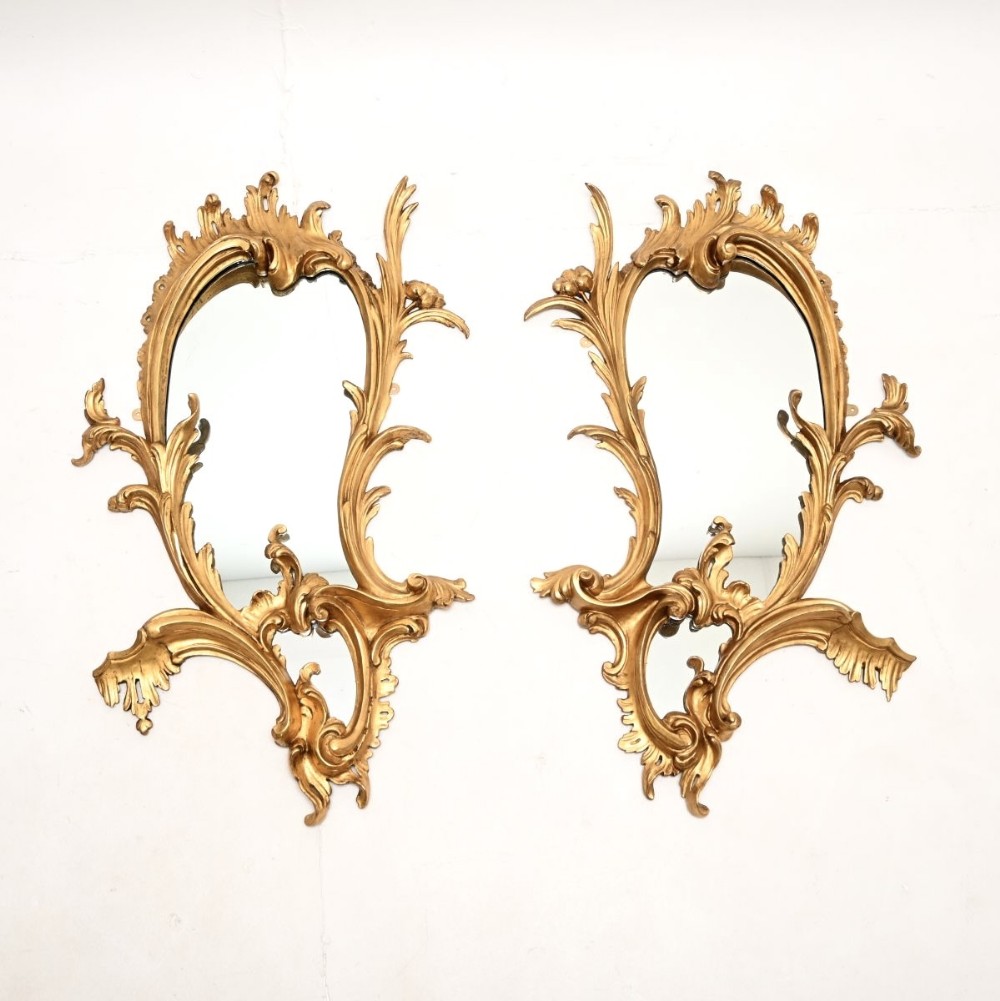 A pair of asymmetrical French Rococo style carved giltwood wall mirrors featuring scrollwork and acanthus leaf detailing.