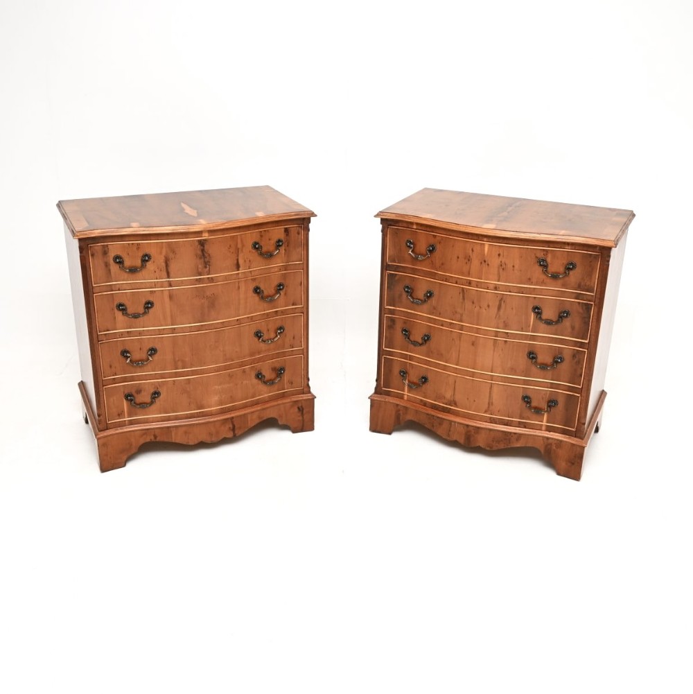 A matching pair of Georgian-style yew wood chests of drawers with serpentine fronts, brass handles, and four drawers each.