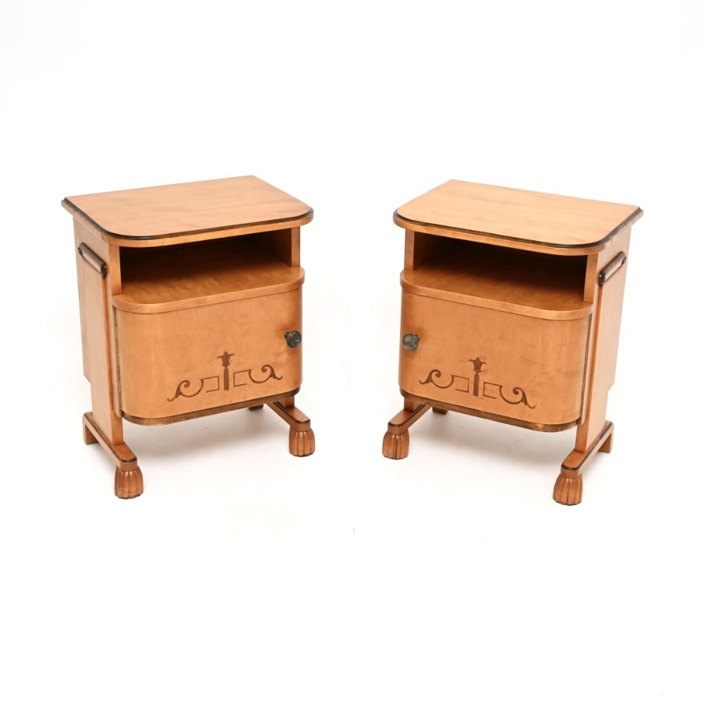 A pair of Swedish Art Deco satin birch bedside cabinets featuring open upper compartments, single inlaid cupboard doors, and carved feet.