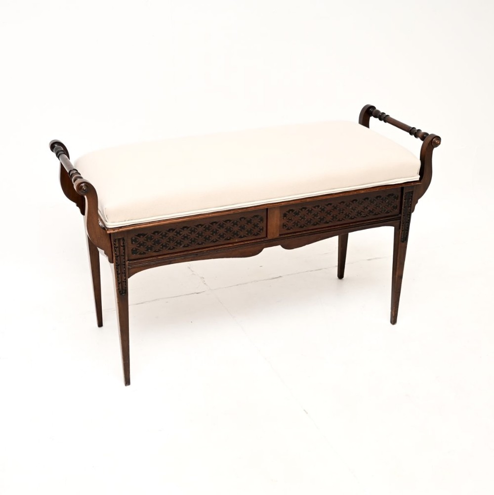 Victorian mahogany duet piano stool featuring cream upholstered seat, turned side handles, pierced fretwork frieze, and square tapered legs.