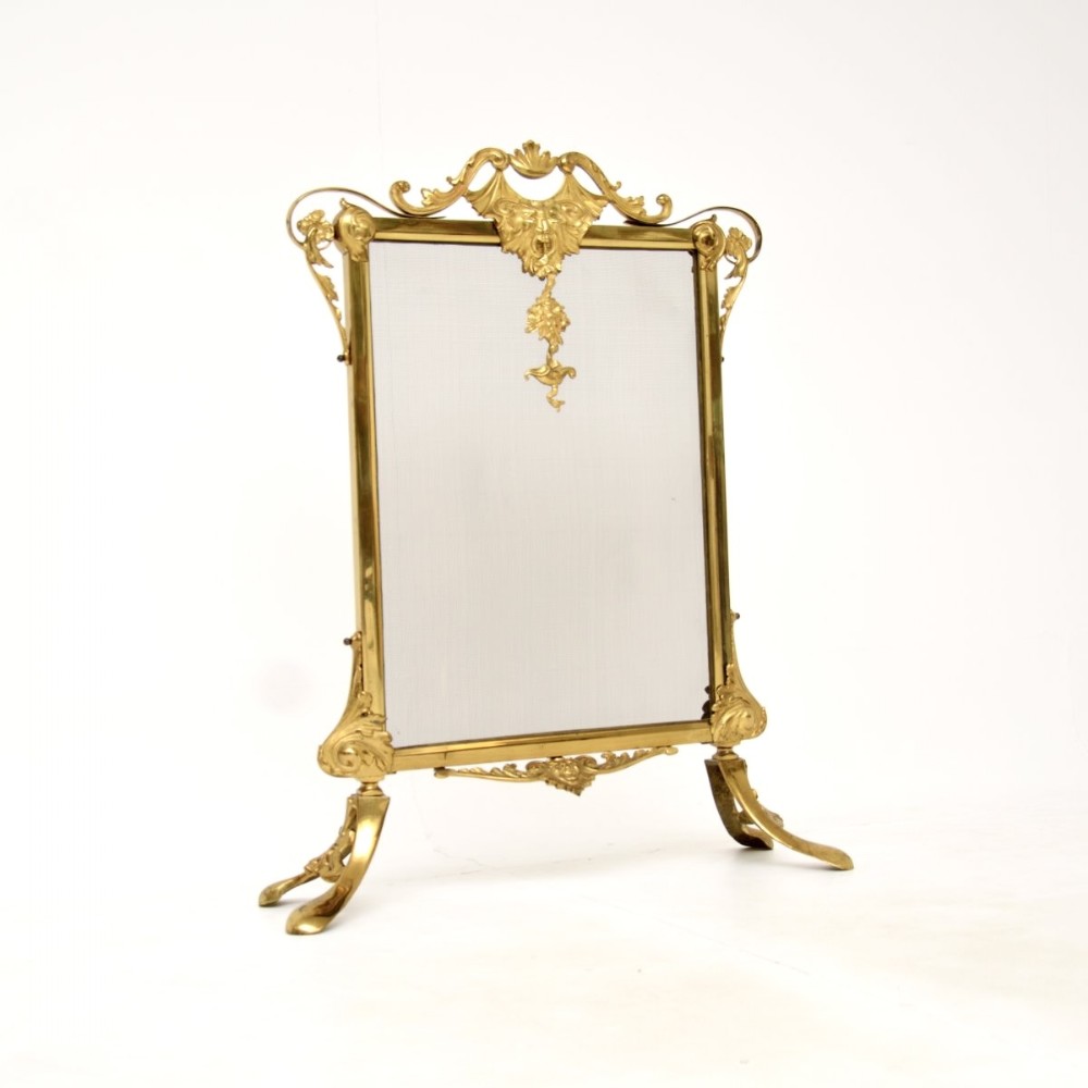 An ornate French gilt metal fire screen featuring a fine wire mesh panel, acanthus scroll cresting, central mask motif, and cabriole feet.