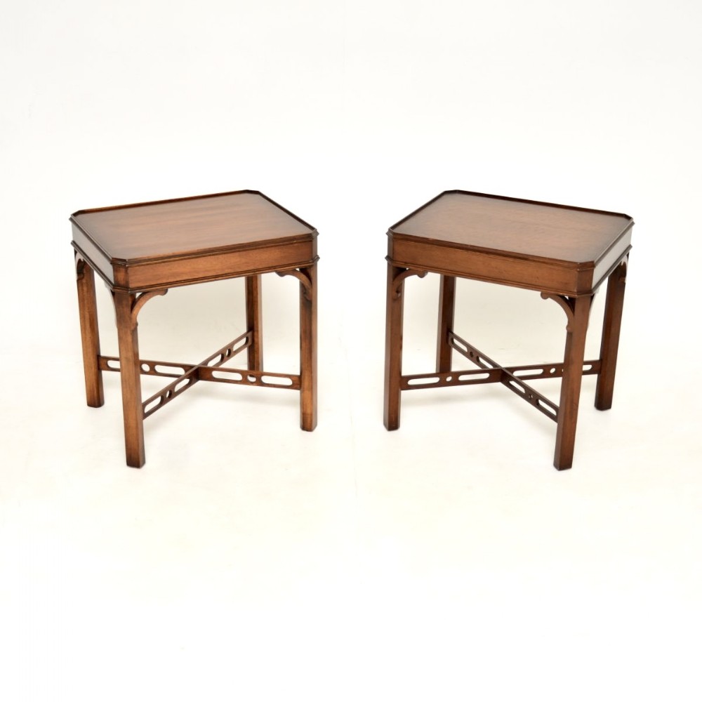 A matching pair of dark mahogany side tables featuring tray-style tops, shaped corner brackets, and pierced X-frame stretchers.