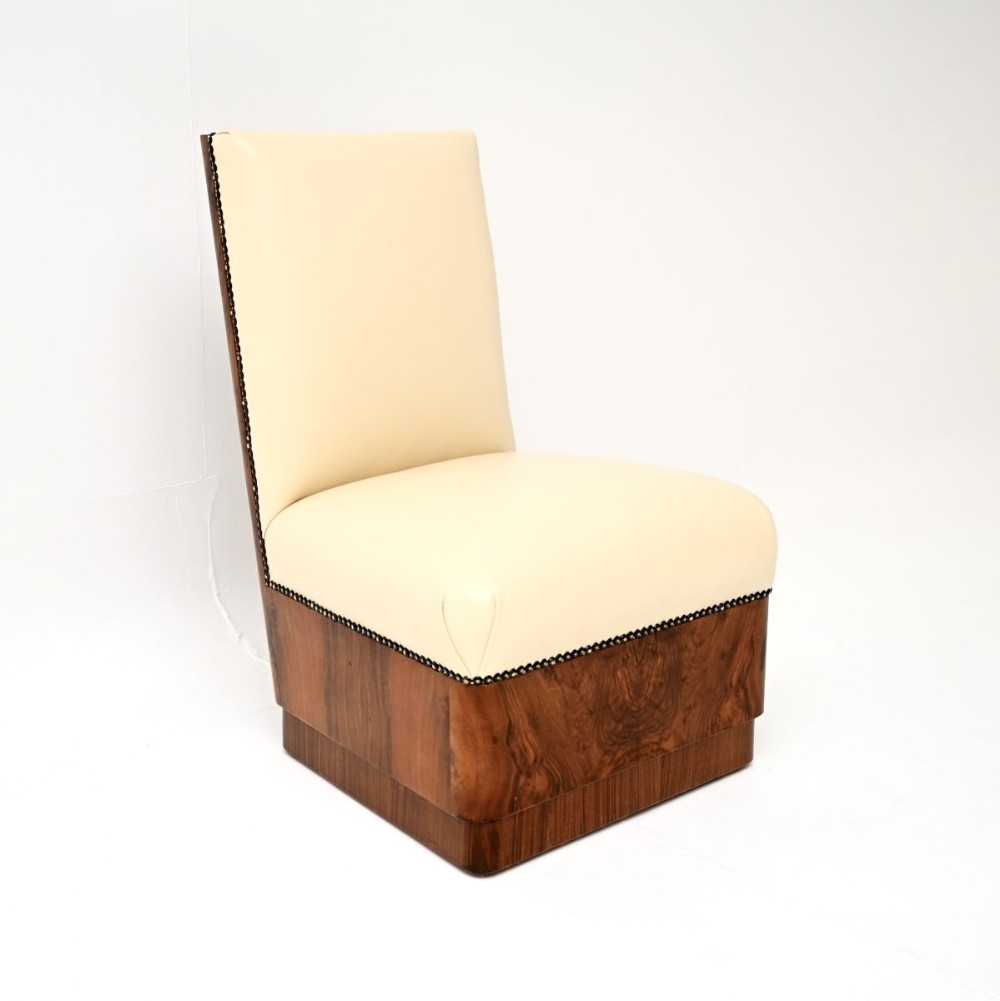 An armless Art Deco side chair upholstered in cream leather with dark stud trim along the edges, supported by a base faced in figured burr walnut veneer.
