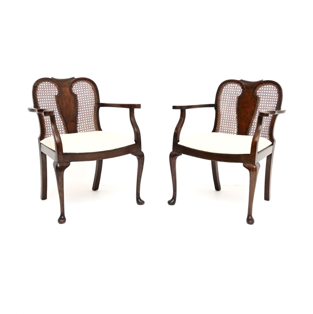 A pair of Edwardian dark walnut armchairs featuring woven cane backs with central wood splats, curved armrests, cabriole legs, and off-white upholstered seats.