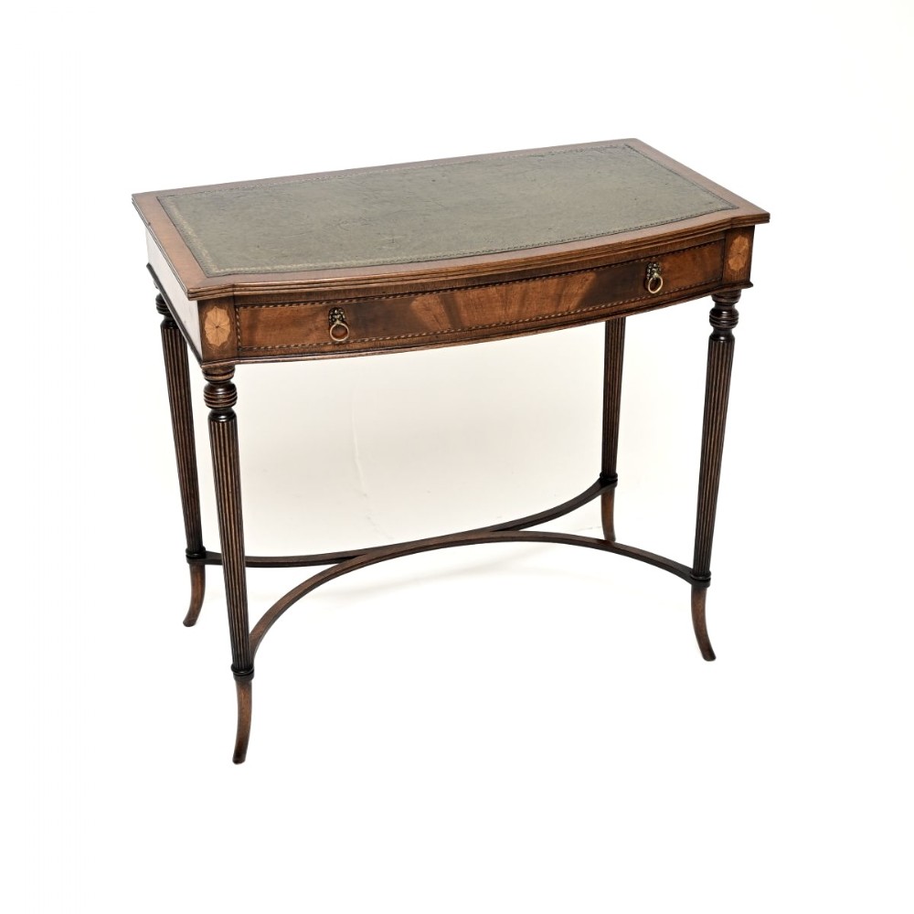 An antique mahogany writing table featuring a green leather top, fine marquetry inlays, a single drawer with ring handles, and slender reeded legs connected by a curved X-stretcher.