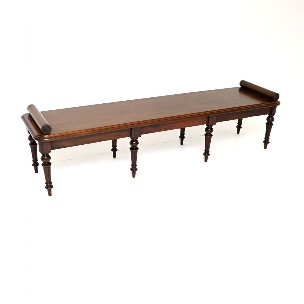 A long antique Victorian mahogany hall bench featuring raised bolster ends and multiple turned legs.