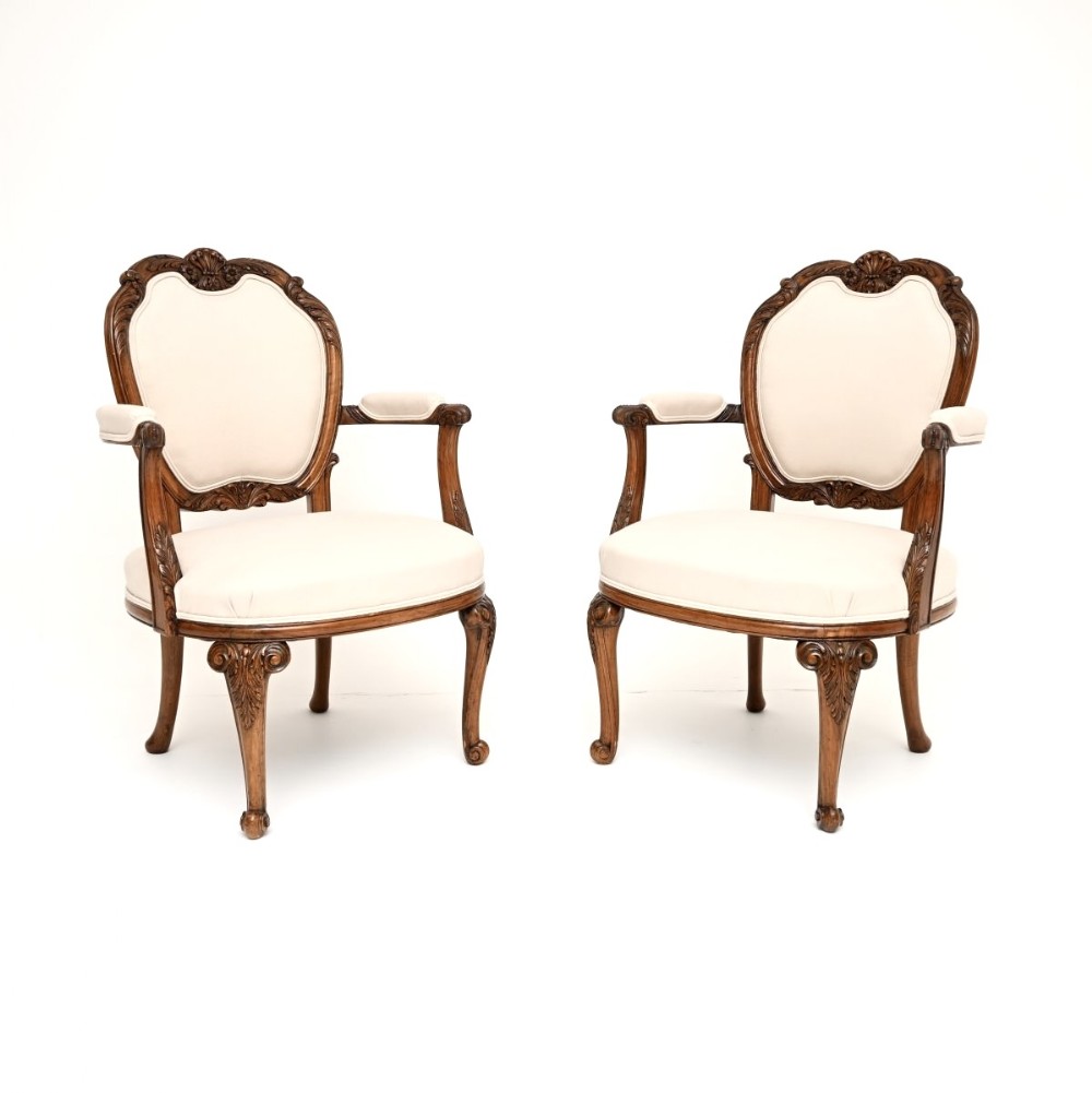 A pair of carved walnut salon armchairs with off-white fabric upholstery and cabriole legs.